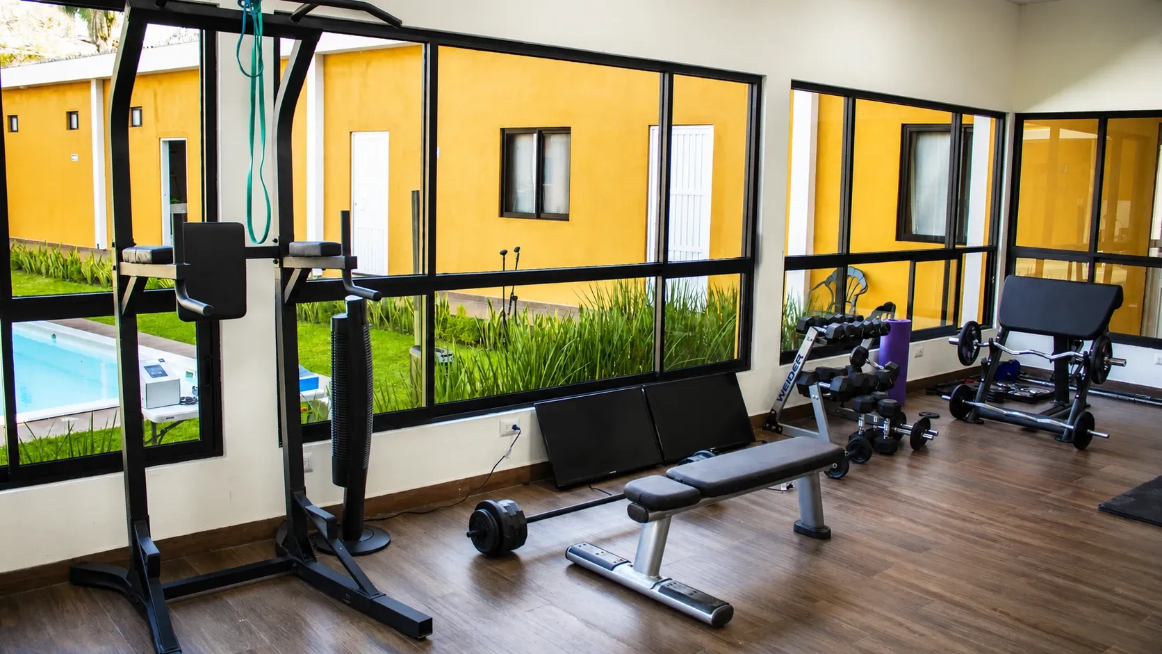 Gimnasio con aparatos y ventanales hacia el jardín