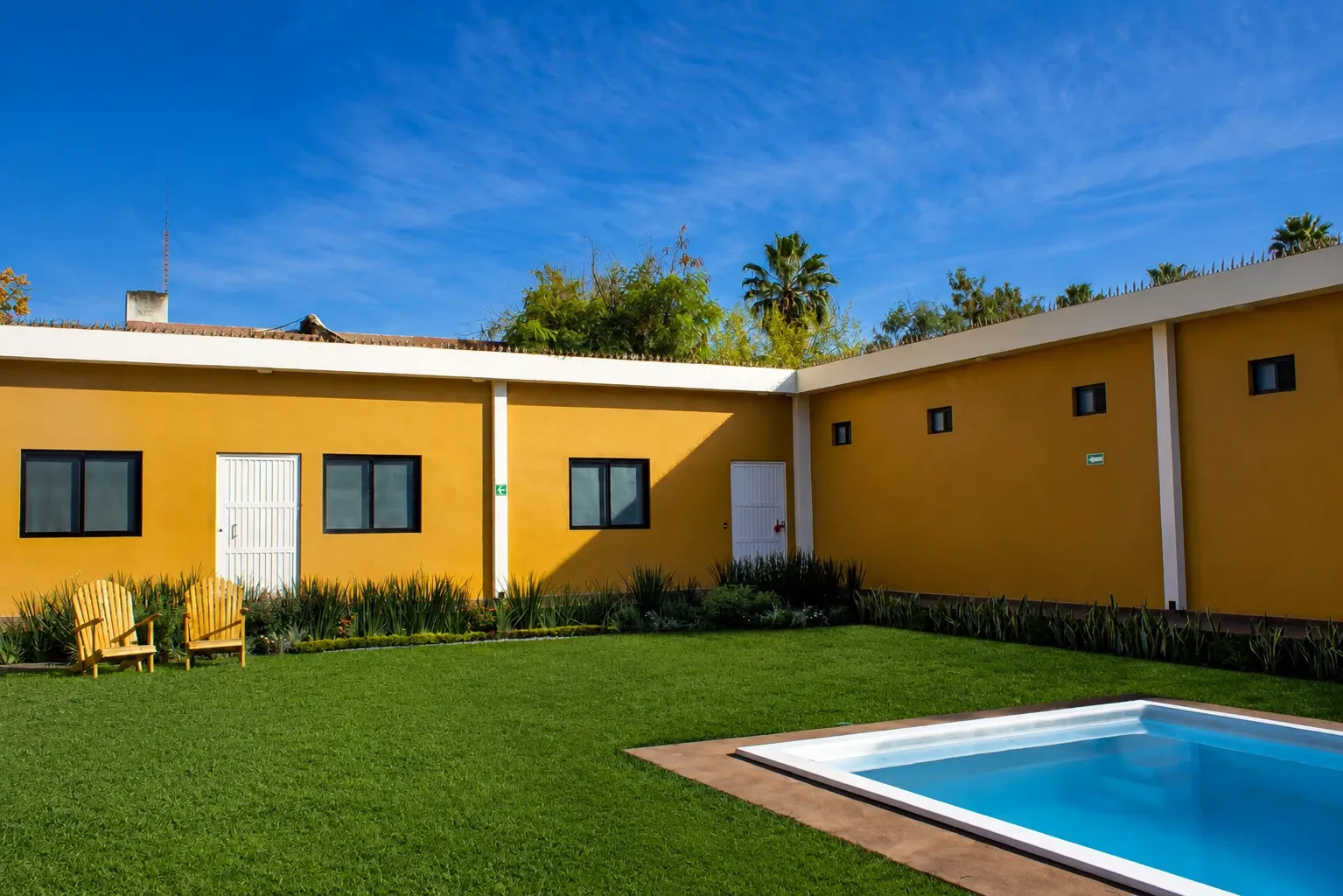Jardín y alberca de la casa Lumenia, con muros amarillos y cielo azul