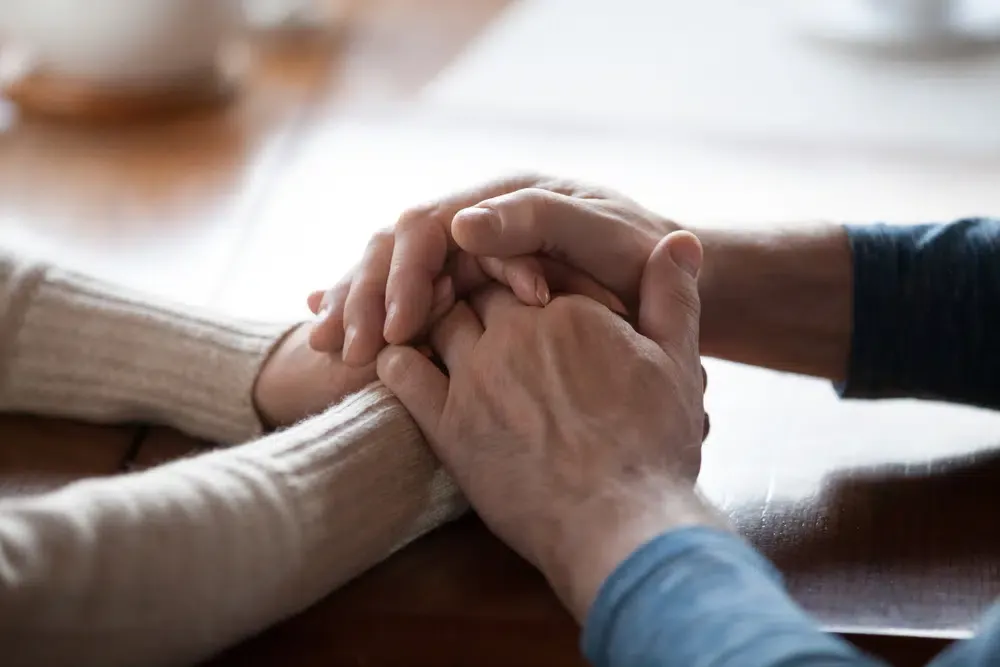 Dos personas se toman de las manos sobre una mesa en señal de apoyo